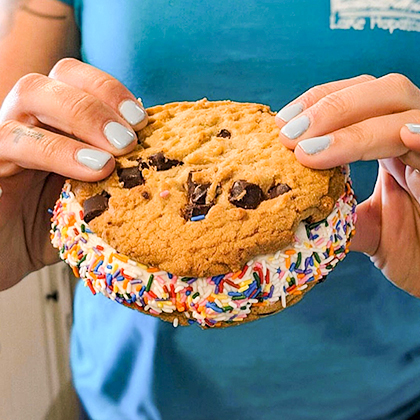Woman holding a chocolate chip cookie ice cream sandwich.