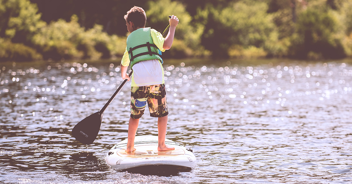 A kid in a life jacket paddling on a surfboard